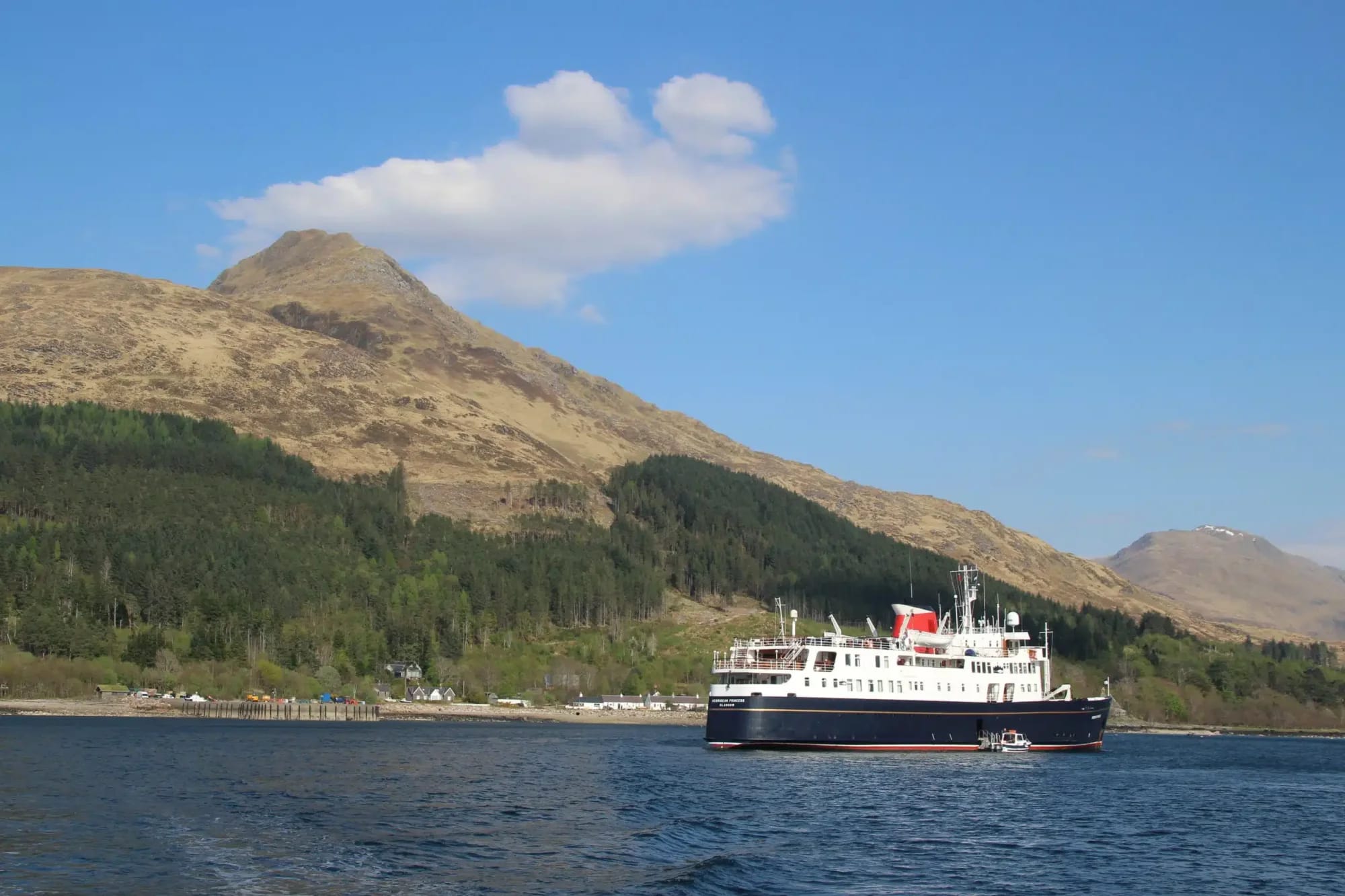 A modern expedition cruise ship anchors in a pristine Scottish loch surrounded by dramatic