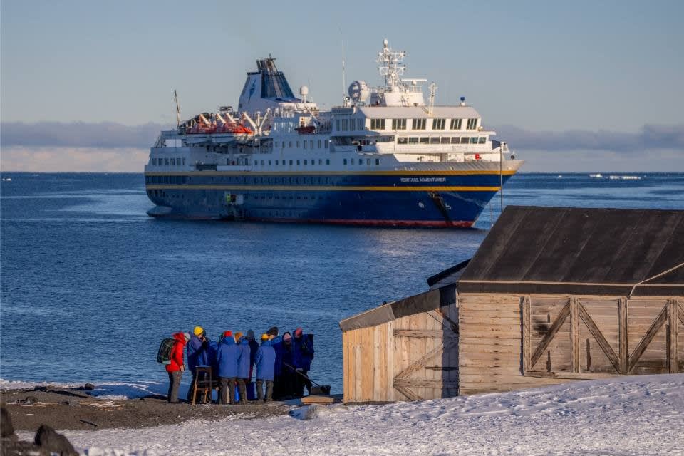 A group of expedition passengers in winter clothing gather on an Arctic beach near a wooden