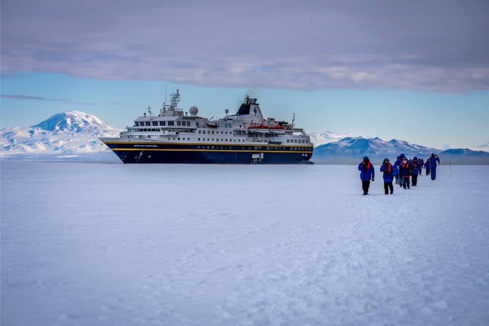A large expedition cruise ship anchored in Antarctic waters with passengers walking across