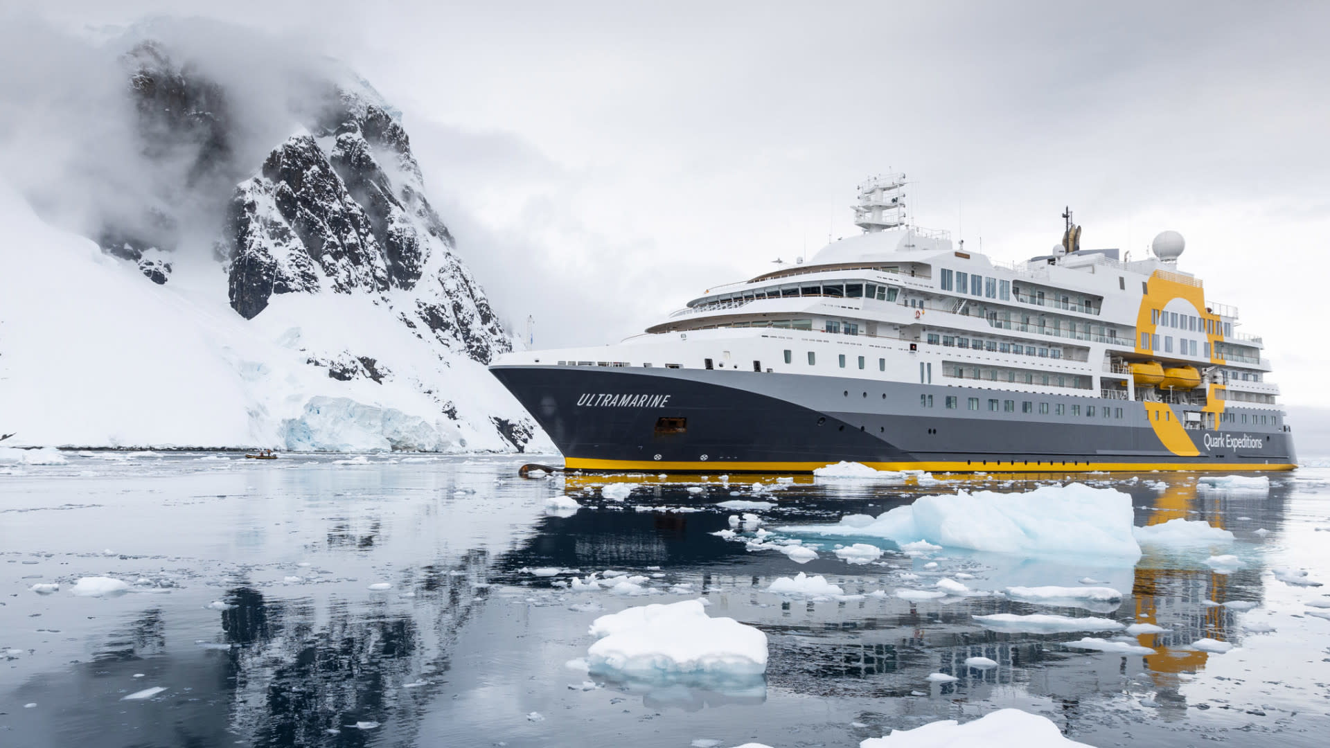 The Ultramarine expedition cruise ship navigating through icy Antarctic waters surrounded by snow-capped mountains and floating icebergs.