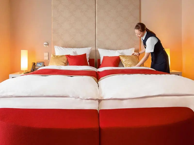 Hotel Room Housekeeping Service Preparation A hotel housekeeper meticulously arranges decorative pillows and bedding on twin beds in a modern