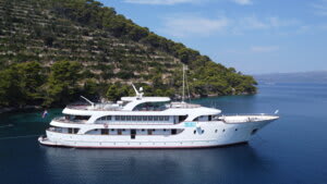 A multi-deck luxury cruise vessel is anchored in pristine turquoise Mediterranean waters adjacent