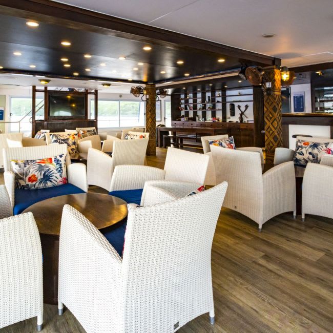 An elegant indoor lounge and bar area aboard a luxury cruise ship, featuring cream-colored wicker