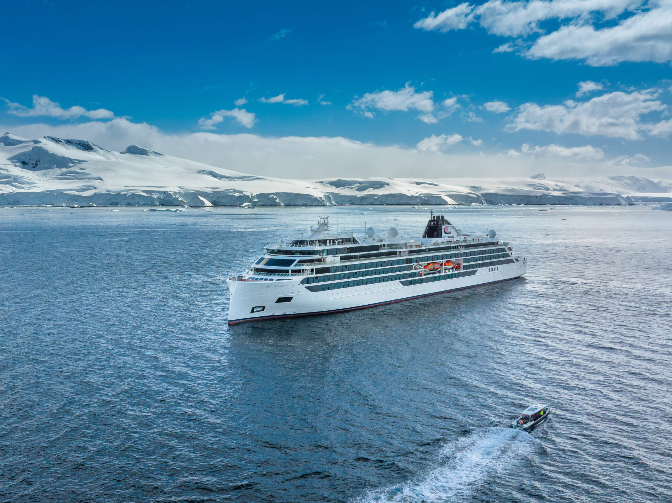 Luxury Cruise Ship in Antarctic Waters A pristine white luxury cruise ship navigating through icy blue waters with snow-covered mountainous Antarctic landscape in the background.