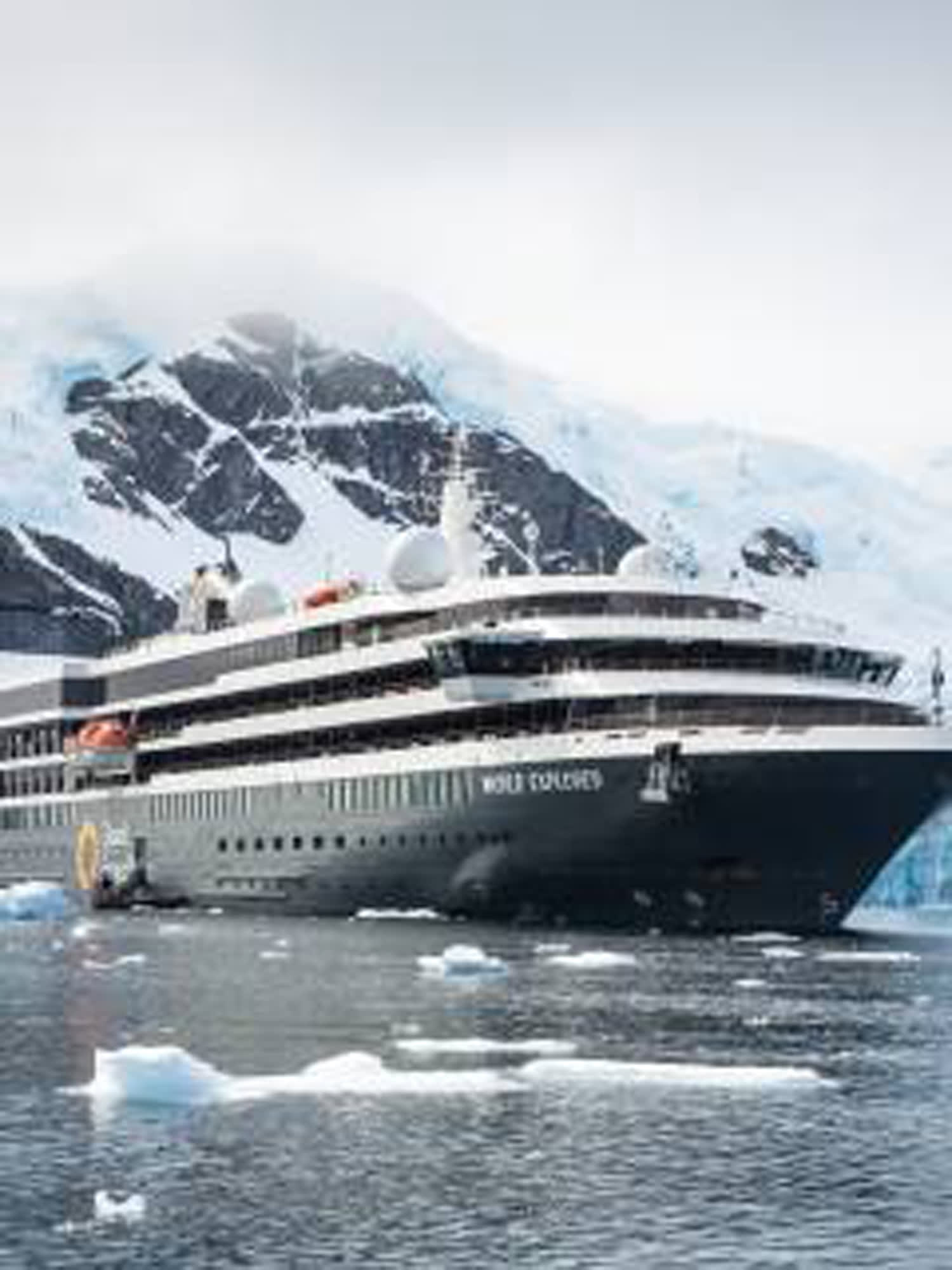 A modern expedition cruise ship navigating through icy waters with snow-capped mountains in