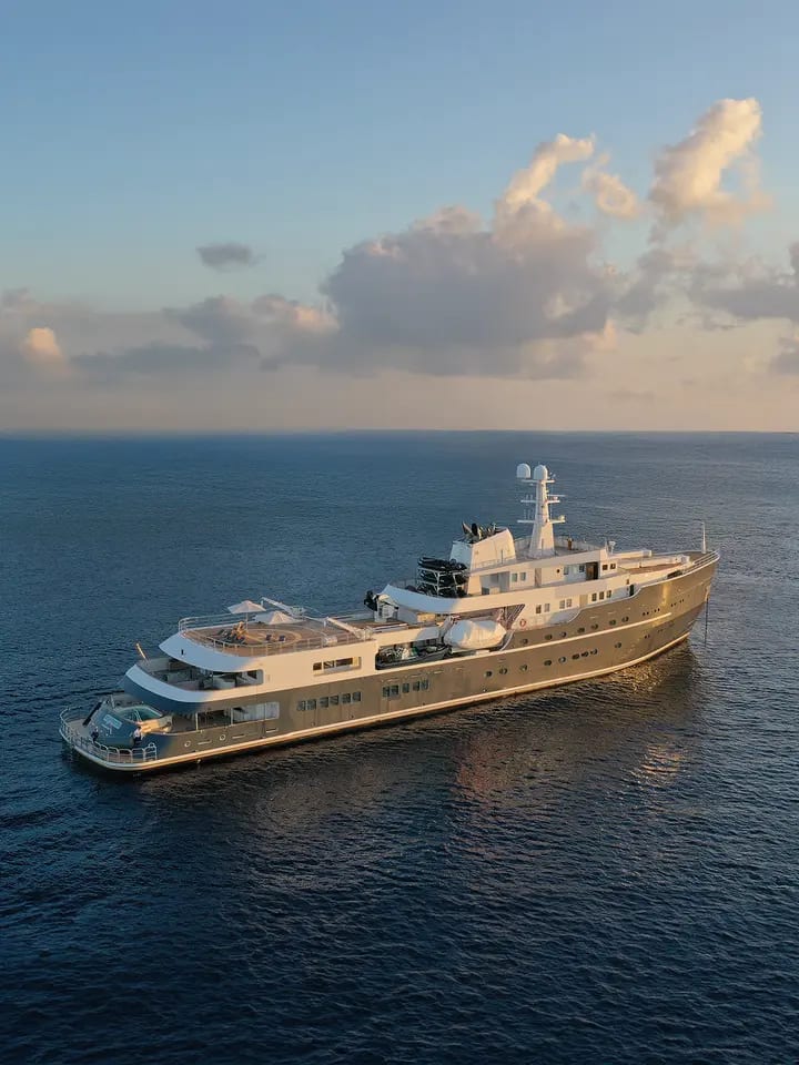 A stunning golden-hulled expedition yacht anchored in calm blue waters during golden hour