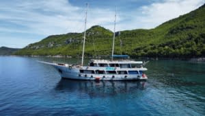 A striking two-masted luxury gulet sailing vessel anchors in crystal-clear turquoise waters