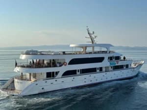 A sophisticated multi-deck motor yacht with white hull and modern architecture cruises through calm