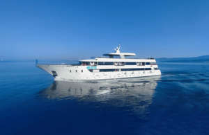 A sleek, white multi-deck motor yacht cruises through crystal-clear azure Mediterranean or tropical