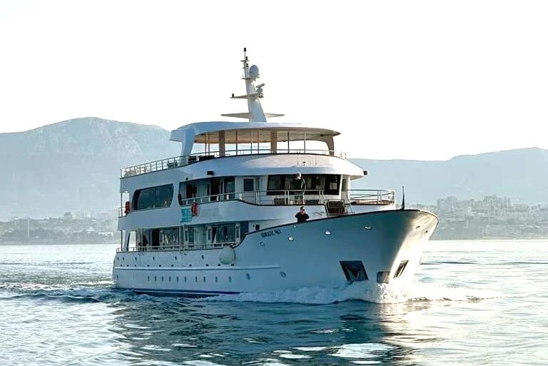 A sophisticated multi-deck motor yacht with light blue and white hull cruising through calm coastal