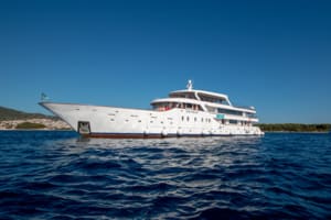 A white luxury motor yacht anchored in crystal-clear blue Mediterranean waters under a clear sky