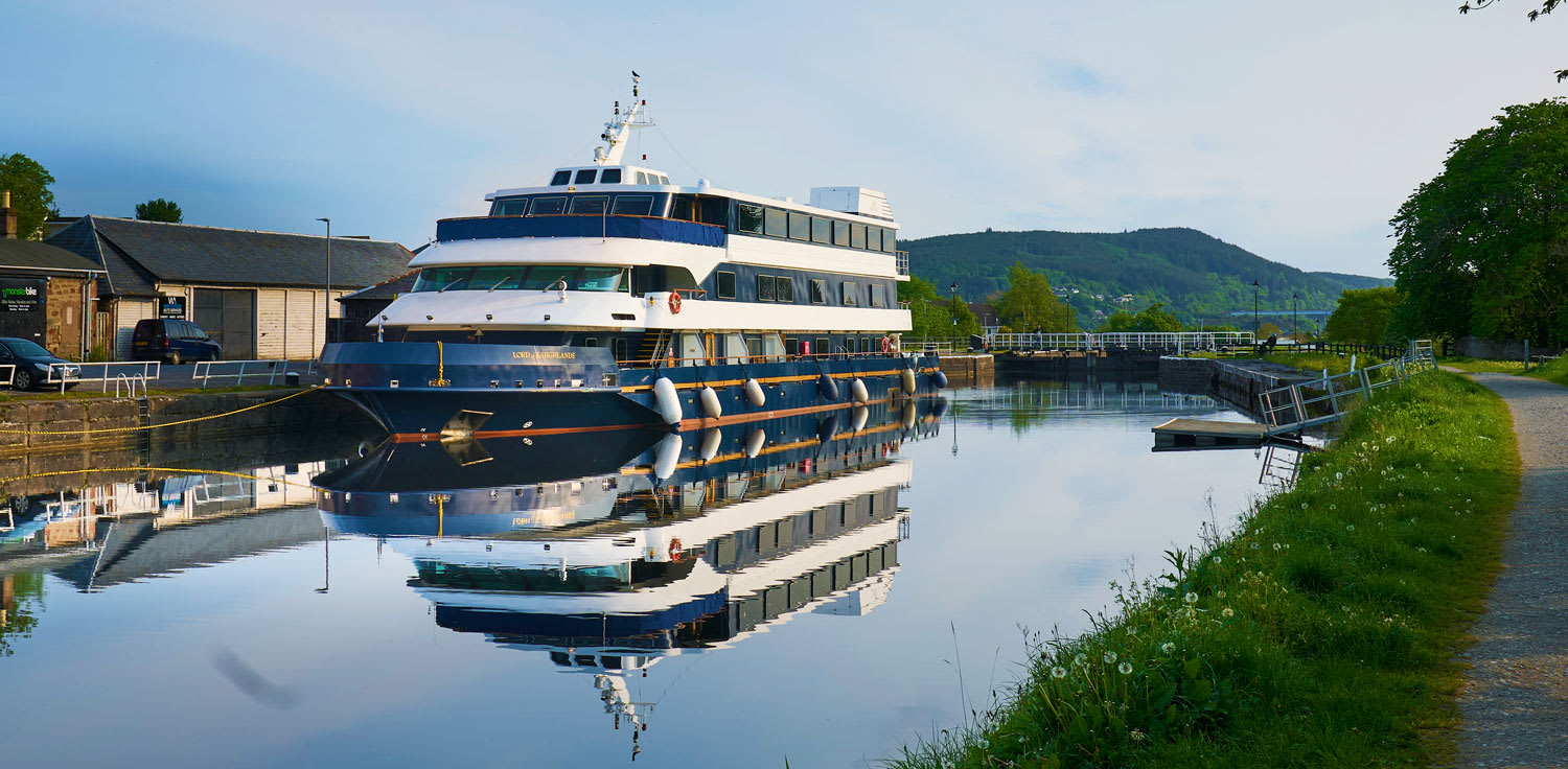 A multi-deck luxury river cruise ship moored at a peaceful inland waterway, featuring distinctive