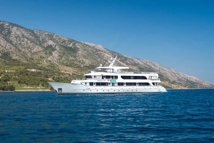 A pristine white luxury motor yacht is anchored in crystal-clear turquoise Mediterranean waters