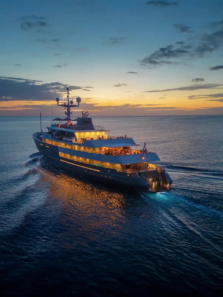 A stunning expedition yacht illuminated by warm golden interior lights anchors in calm waters