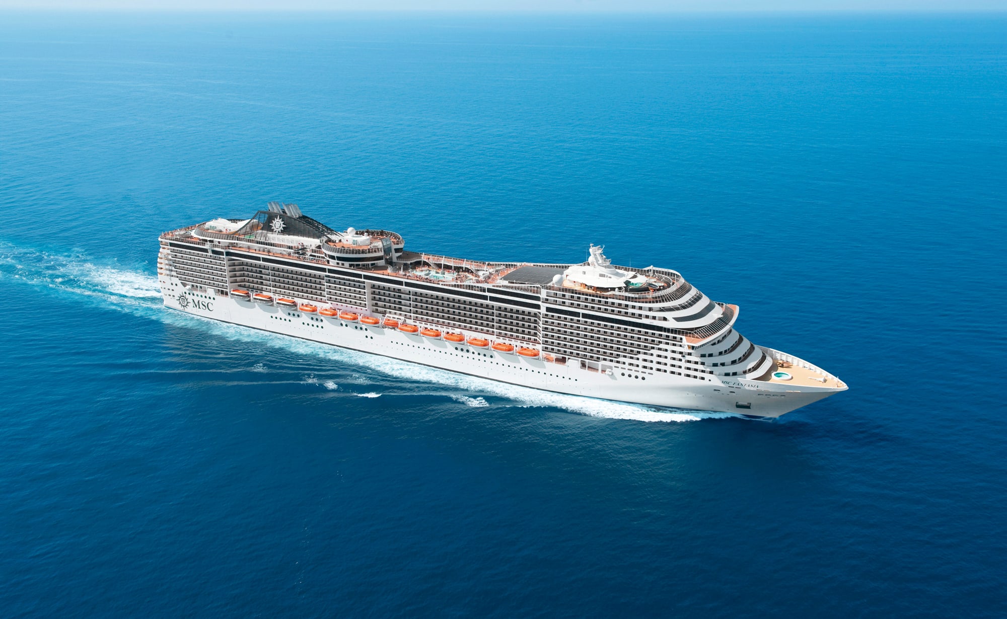 A large white and gray MSC cruise ship sailing through vibrant blue ocean waters, showcasing
