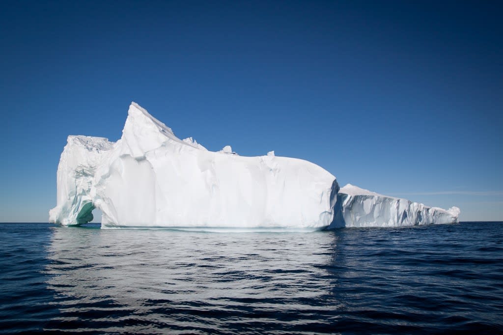A large, sculptural iceberg with brilliant white peaks and turquoise-tinted crevices floats in deep