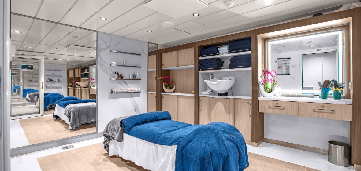 A luxurious and contemporary cruise ship cabin featuring a spacious bedroom with blue bedding, integrated marble bathroom, and clever built-in storage solutions.