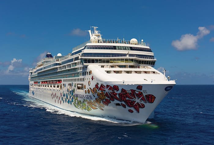 Norwegian Gem Cruising Blue Waters A colorful Norwegian Cruise Line ship sailing across a bright blue ocean with a clear sky and white clouds in the background. The ship features a distinctive artistic hull design with colorful graphics.