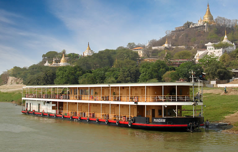 A multi-deck river cruise boat named Pandaw navigating a river in Myanmar with golden Buddhist