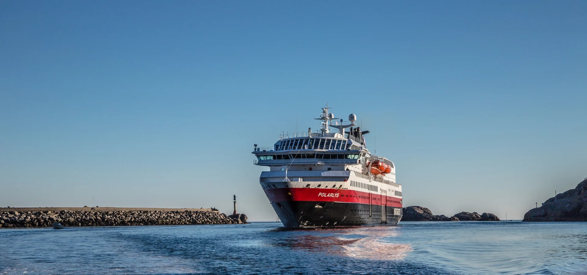 Polaris Cruise Ship in Coastal Harbor A modern cruise ship with red and white livery named Polaris navigating through a rocky coastal harbor with calm blue waters and clear sky.
