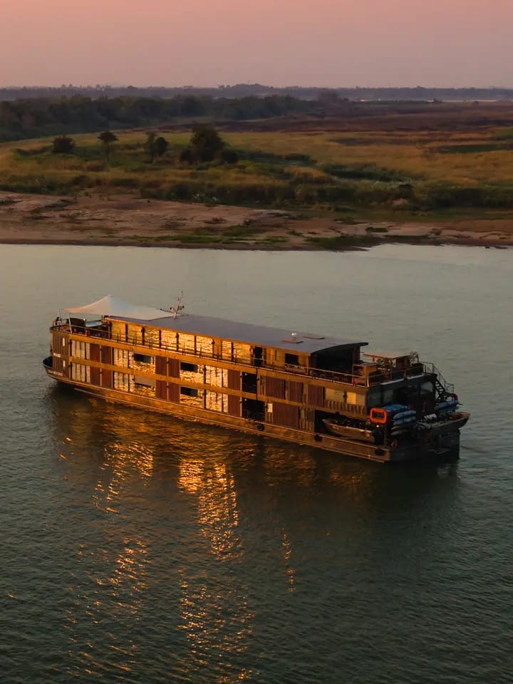 A luxurious river cruise vessel with distinctive golden-lit wooden architecture floats peacefully