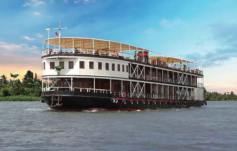 A multi-deck river cruise ship navigating through a lush tropical river landscape with verdant