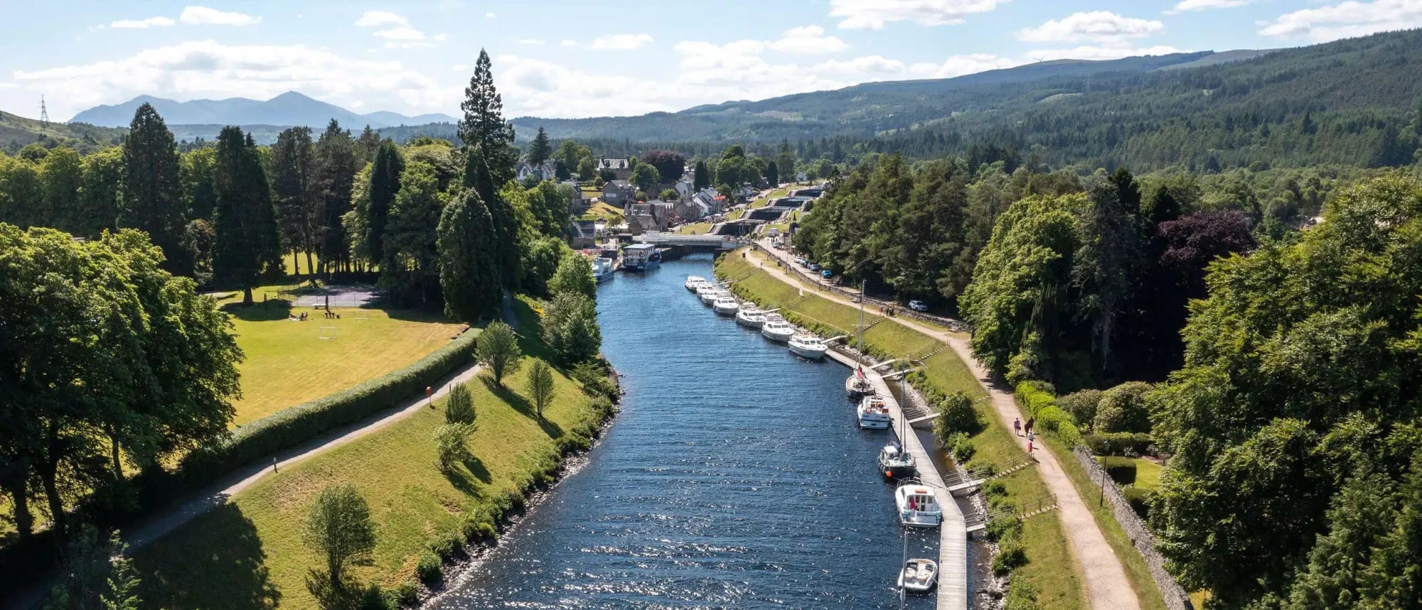 An idyllic riverside town nestled in a forested valley with numerous pleasure boats and small