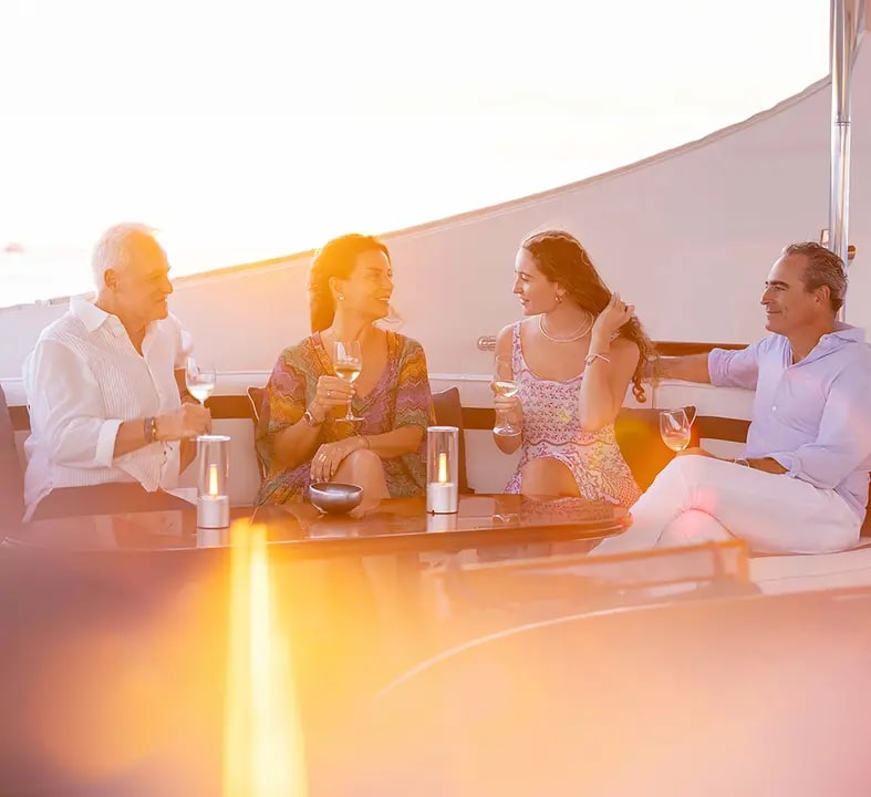 Four well-dressed guests enjoy cocktails and conversation on an upper deck of a cruise ship during