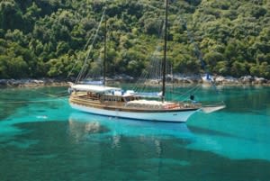 A classic wooden gulet sailing vessel anchors in crystal-clear turquoise waters near a lush