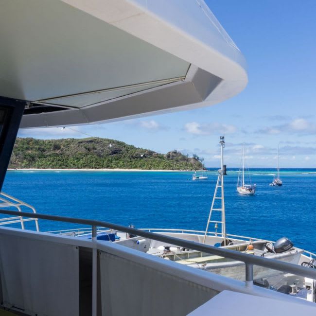 A scenic view from a cruise ship's deck showing multiple sailboats anchored in crystal-clear