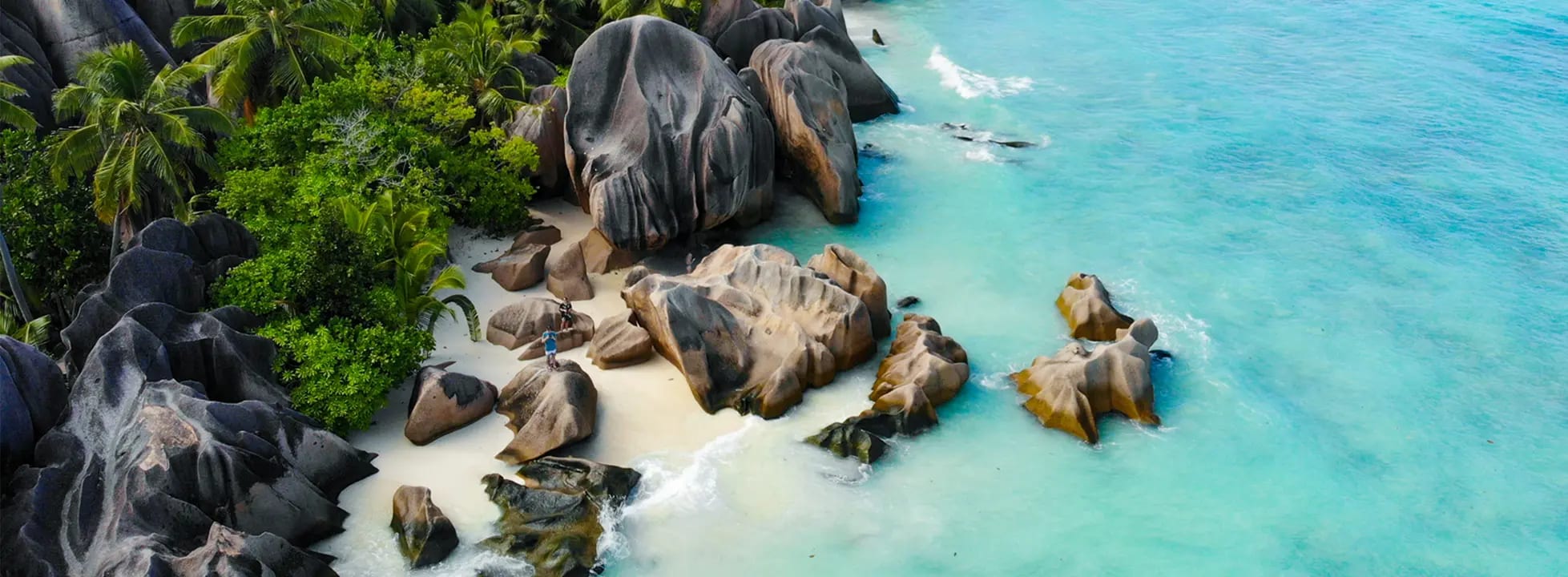 A stunning tropical beach cove featuring distinctive large granite boulders scattered across