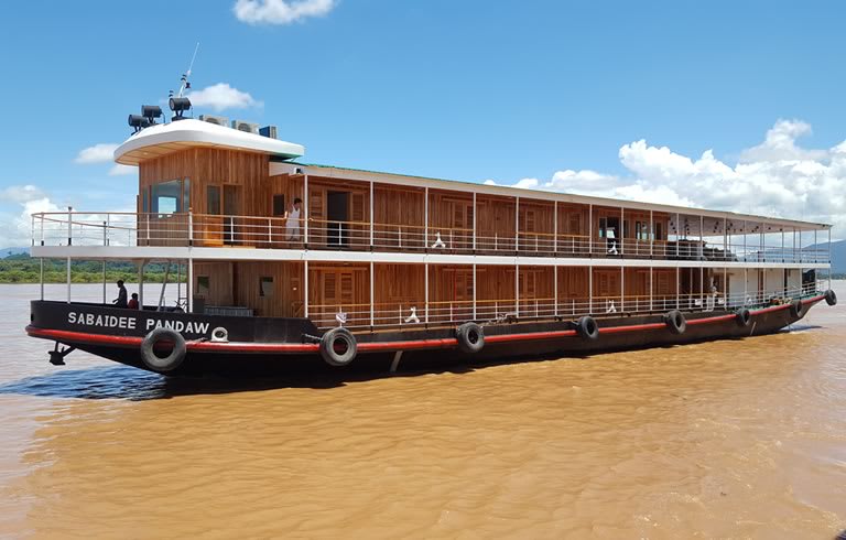 A two-deck wooden river cruise boat named 'Sabaidee Pandaw' sailing on a muddy brown river with