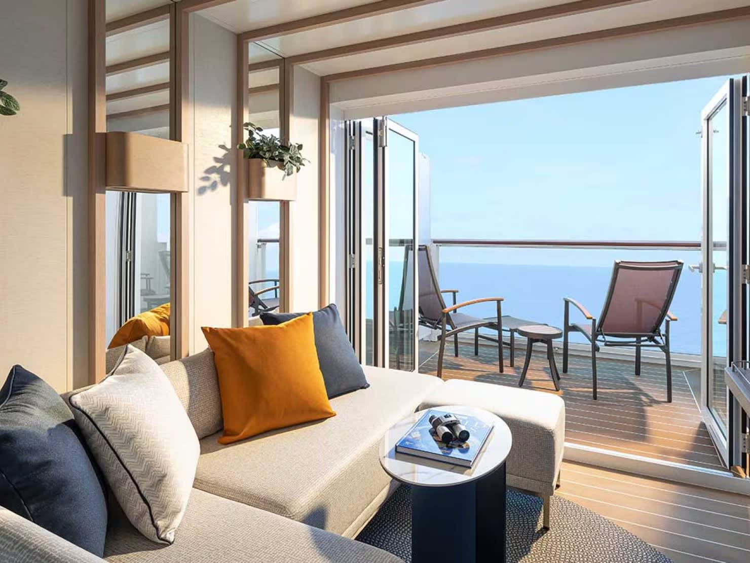 accommodation-balcony-view-sofa-cabin-pocjpgimage14801110high A luxurious modern cabin suite featuring a comfortable sofa with orange and gray pillows, offering expansive ocean views through floor-to-ceiling windows and sliding glass doors that open onto a private balcony with lounge seating.