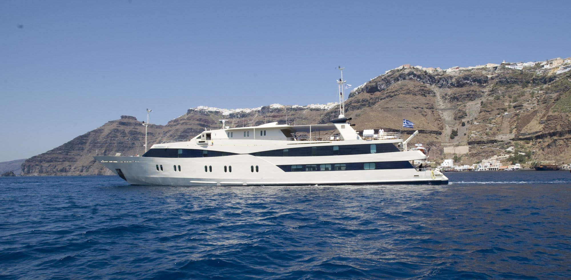 Luxury yacht anchored off Santorini with whitewashed buildings and volcanic cliffs in the background