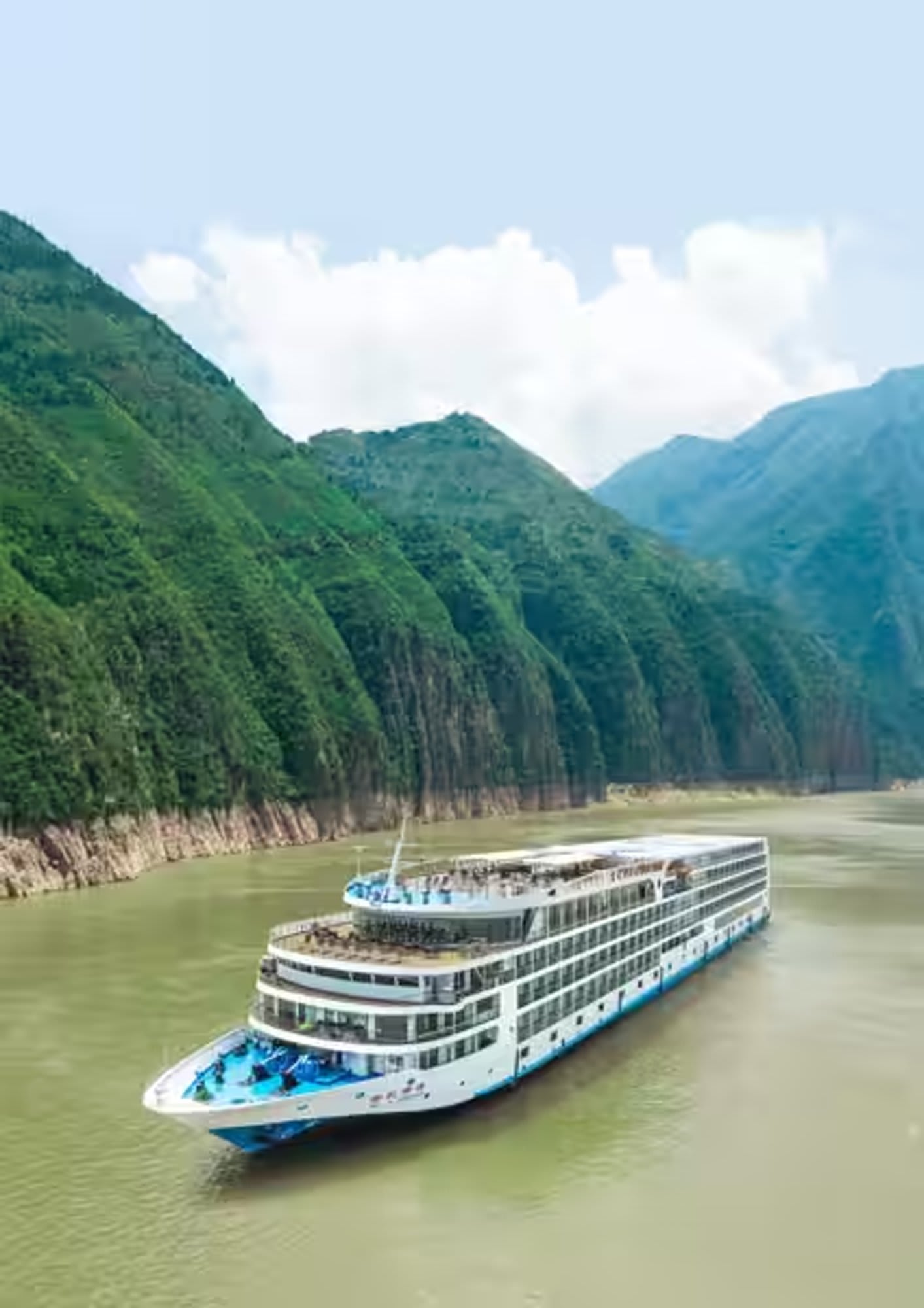 A modern river cruise ship navigates through a scenic gorge with dramatic green-forested mountains rising steeply on both sides and misty peaks in the distance.
