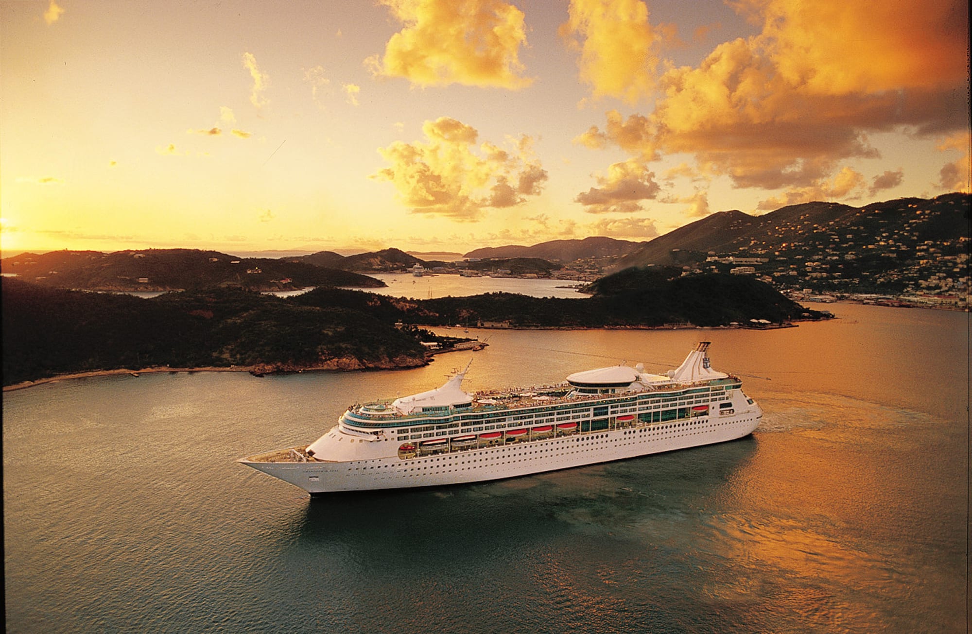 Cruise Ship Anchored in Tropical Island Waters at Sunset A large modern cruise ship is anchored in calm tropical waters during golden hour, with lush green
