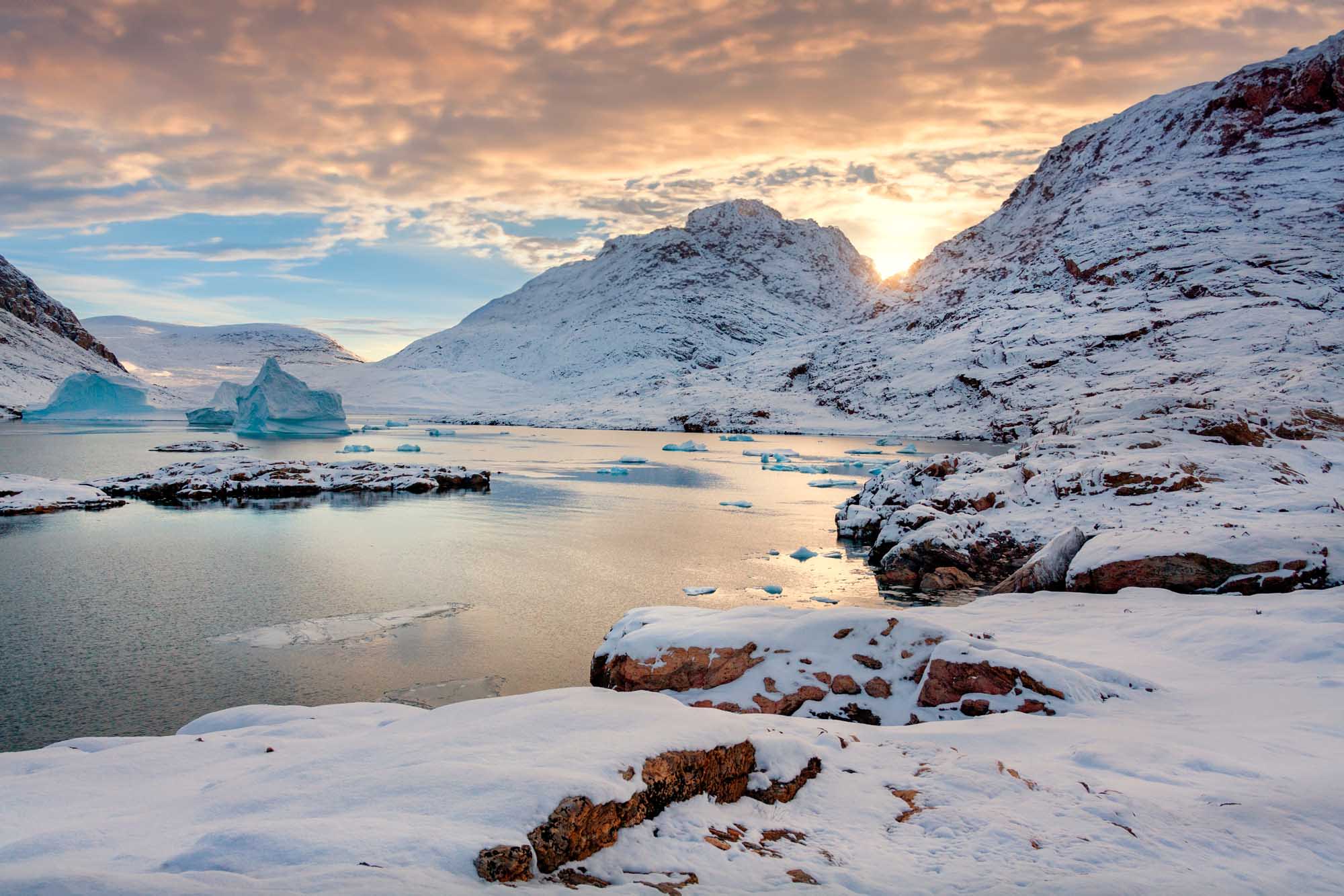 A stunning Arctic landscape featuring snow-covered mountains framing a frozen inlet dotted