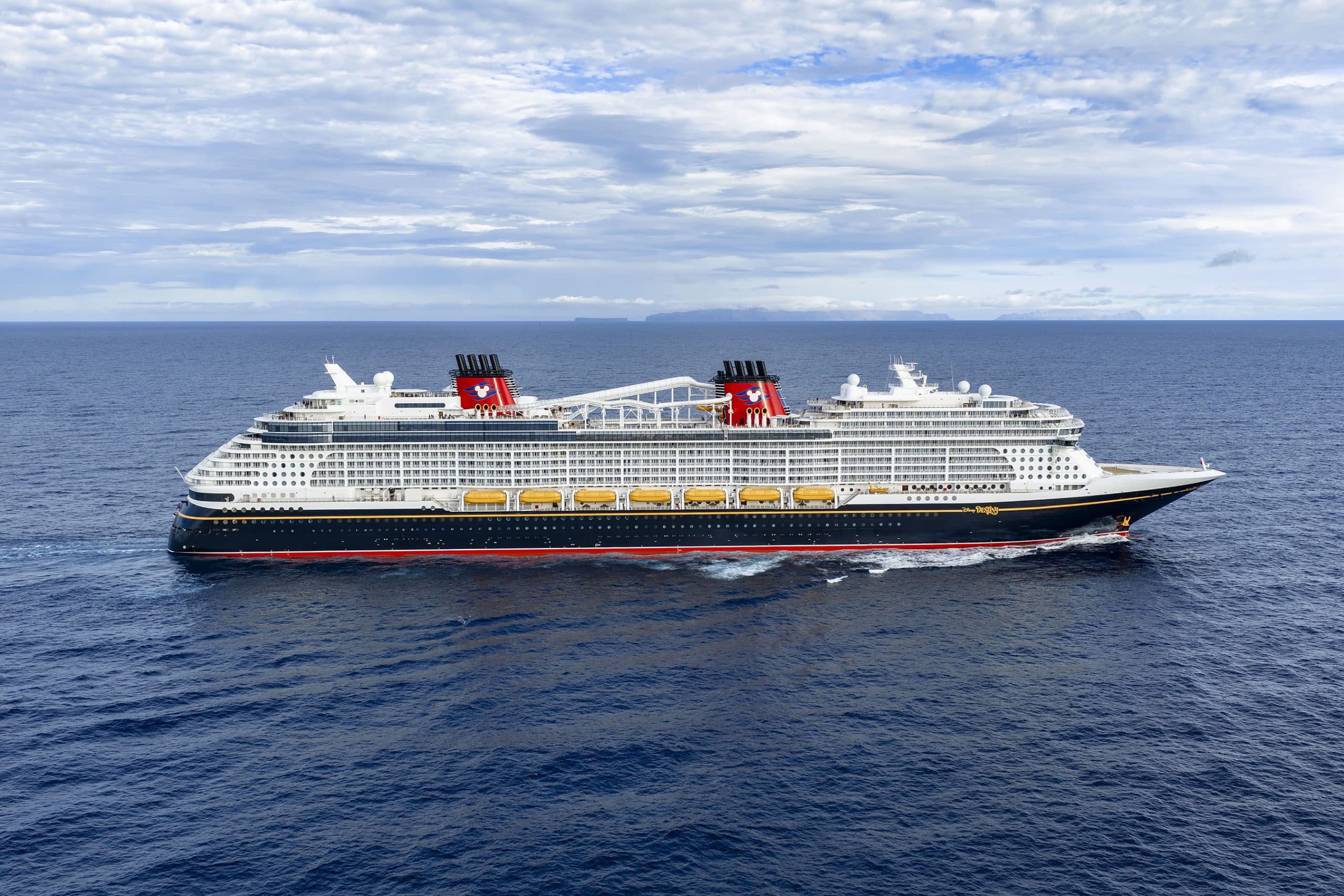 Large Cruise Ship at Sea with Mountains A large Disney cruise ship at sea with mountains in the background under clear skies.