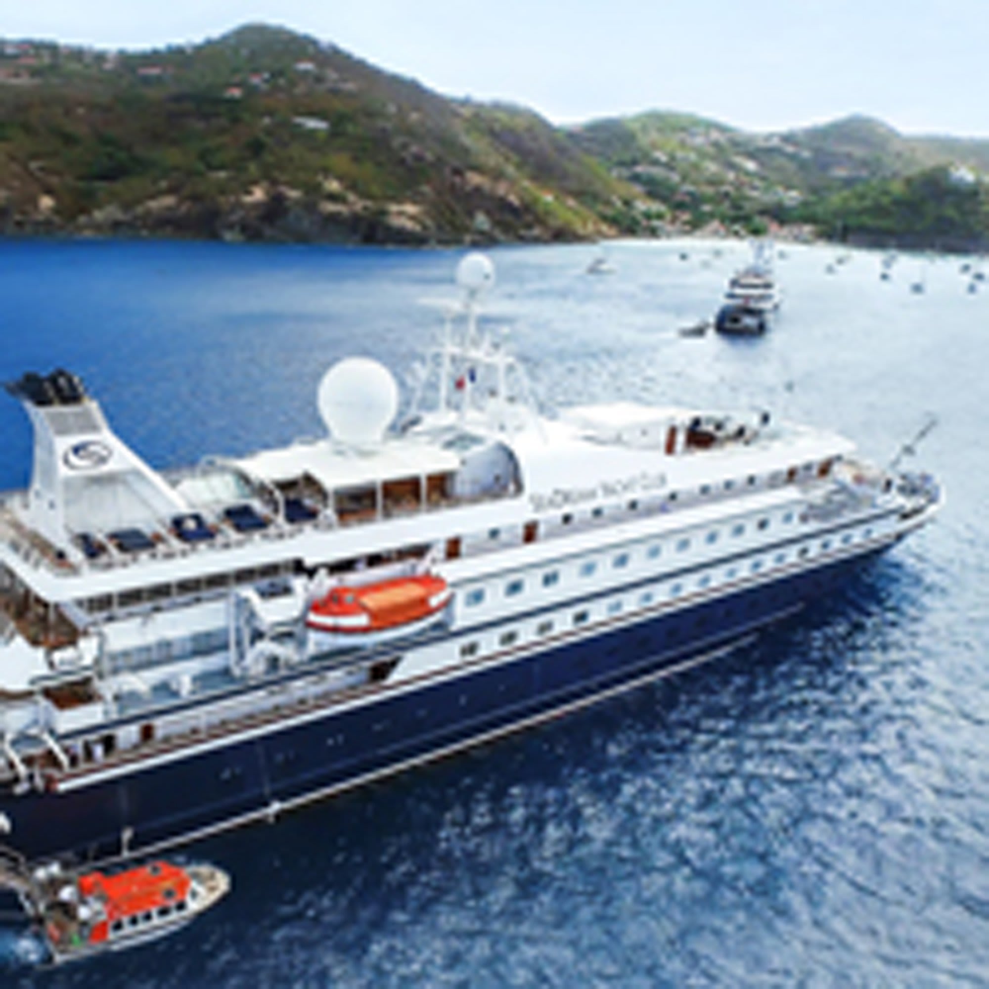 Luxury Cruise Ship Anchored in Adriatic Bay A large expedition cruise ship with distinctive dark hull and white superstructure is anchored in crystal-clear turquoise waters off a scenic Mediterranean coastal town.