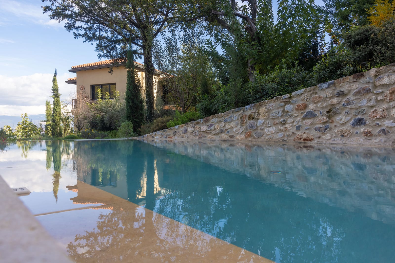 Eup_0654 Tuscan villa with terracotta roof beside infinity pool and stone wall, surrounded by cypress trees