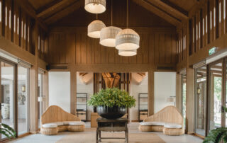 Modern spa lobby with wooden ceiling, pendant lights, woven seating, and central plant arrangement