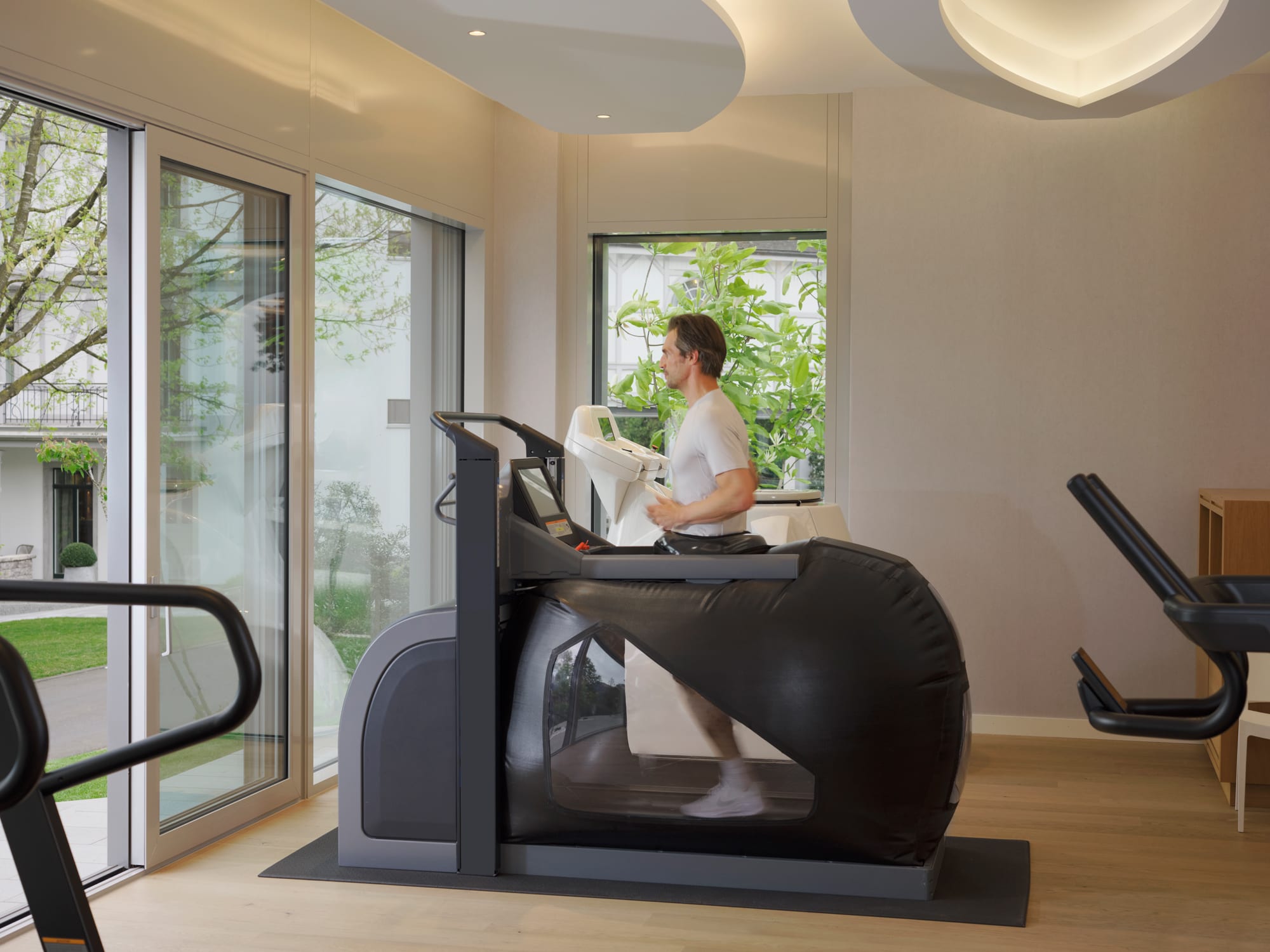 240501_Chenot Palace Weggis_DSCF7370 Man using elliptical machine in modern home gym with curved ceiling and garden views
