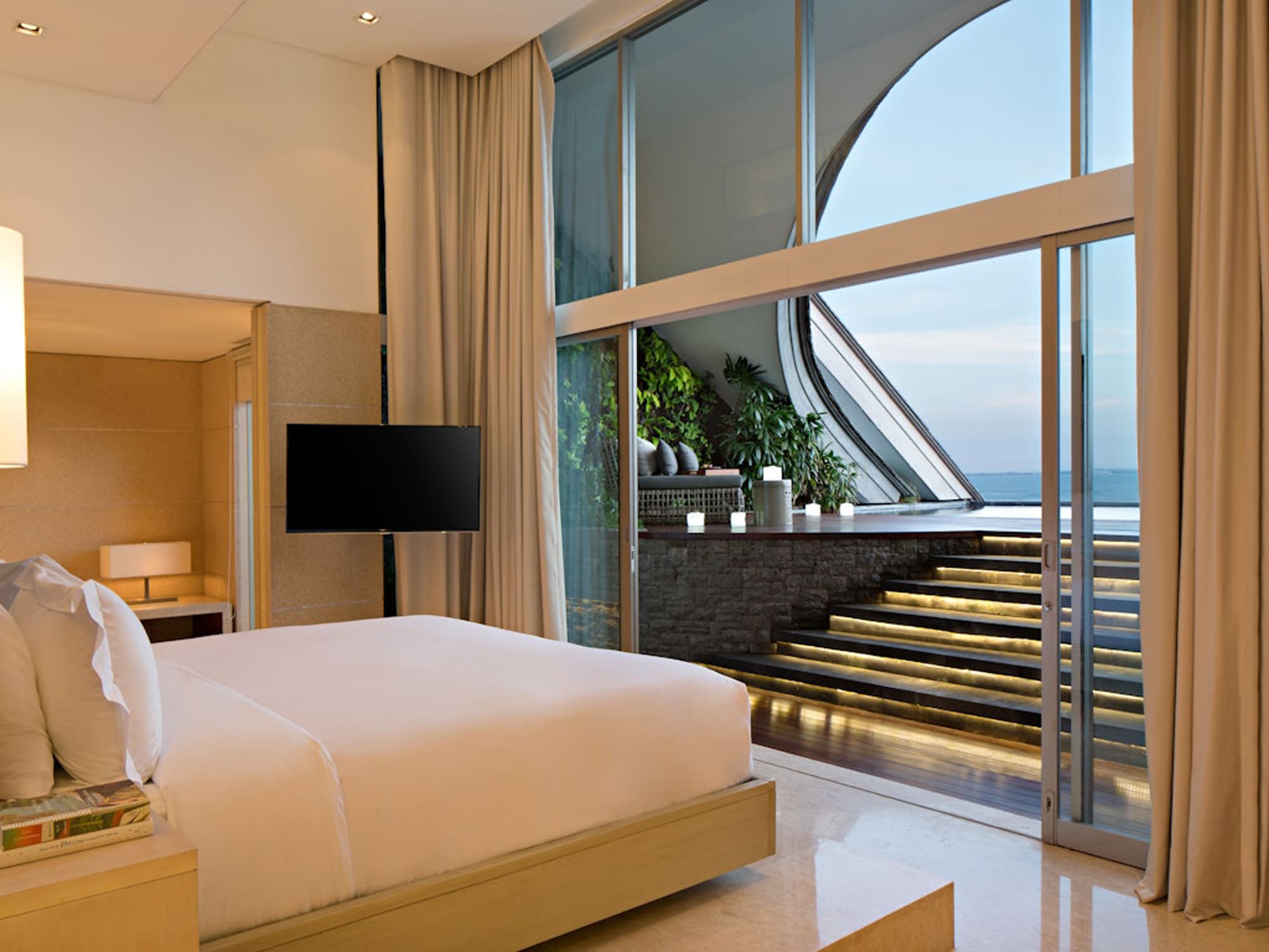 COMO_Uma_Canggu_COMO_Penthouse_Master_Bedroom_1_Medium Modern hotel penthouse bedroom with ocean view, curved floor-to-ceiling windows, and contemporary furnishings