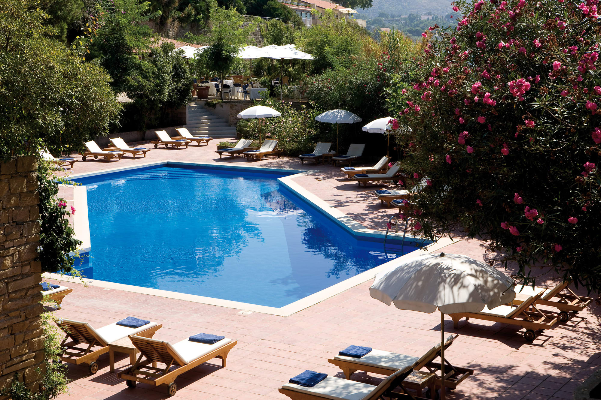 Copy of Copy of Pool (1) Resort swimming pool surrounded by lounge chairs, pink flowering bushes, and white umbrellas in hillside garden