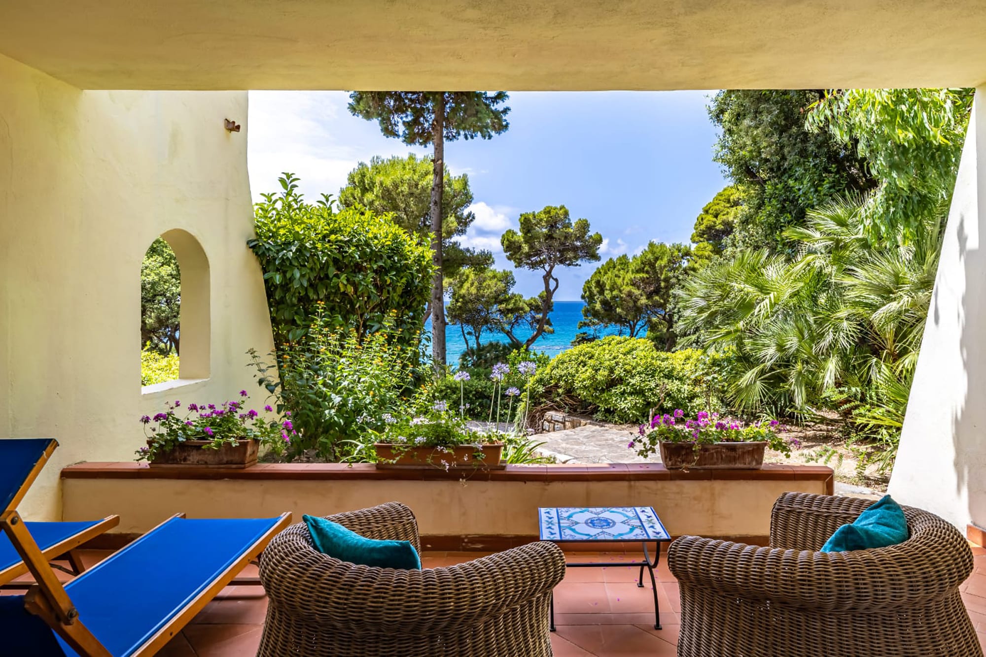 Copy of view from ground floor in villas Mediterranean patio with wicker chairs overlooking turquoise sea and pine trees