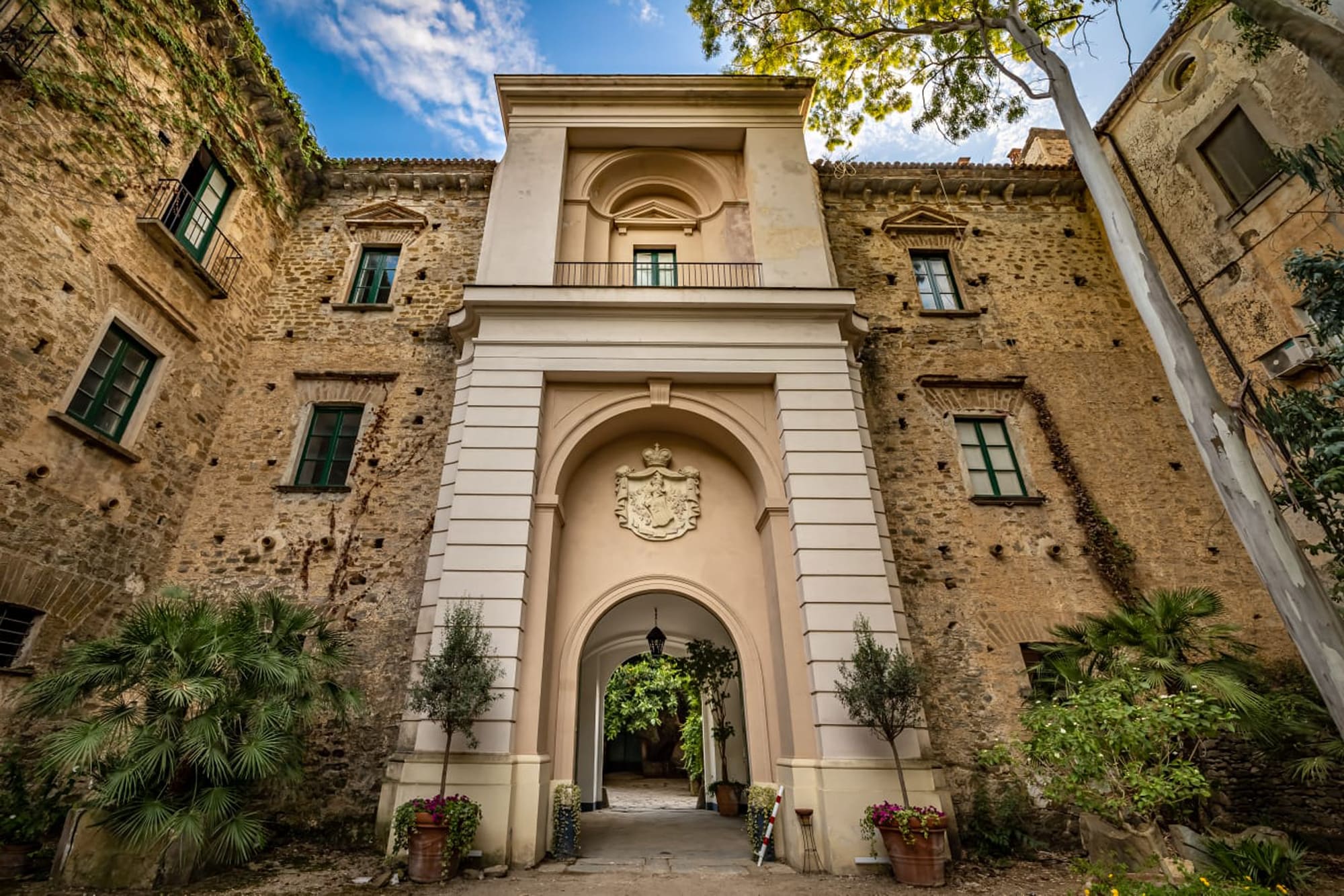 Entrance at Palazzo Historic stone palazzo entrance with cream-colored neoclassical facade and heraldic crest above arched doorway