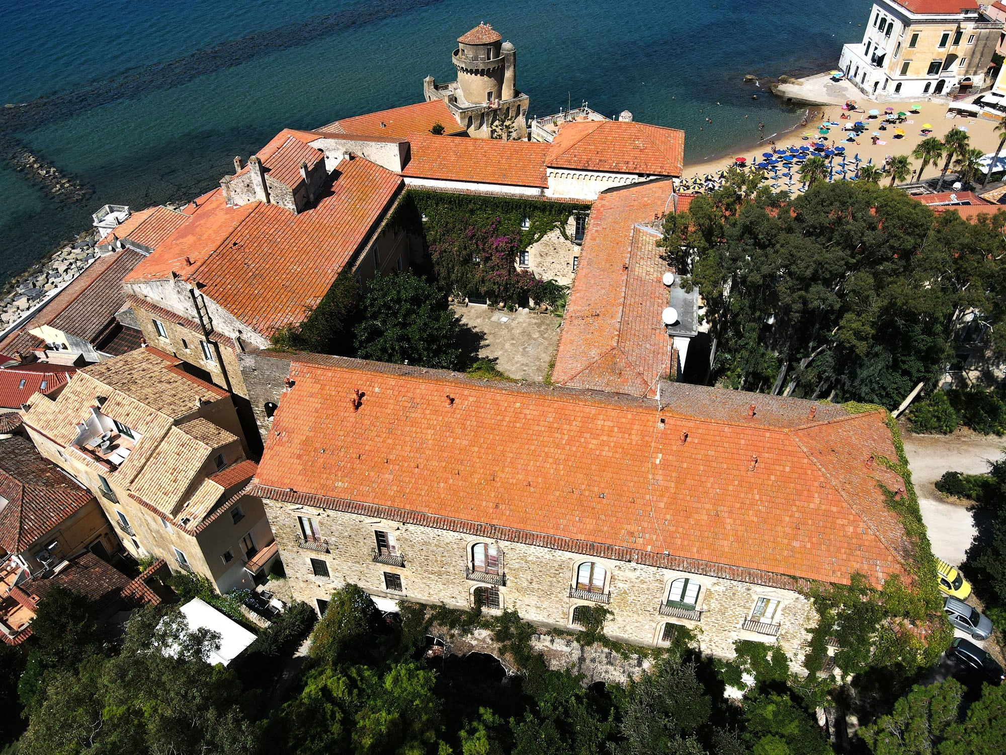 Overview Aerial view of Italian coastal village with terracotta-roofed buildings, tower, and beach with umbrellas