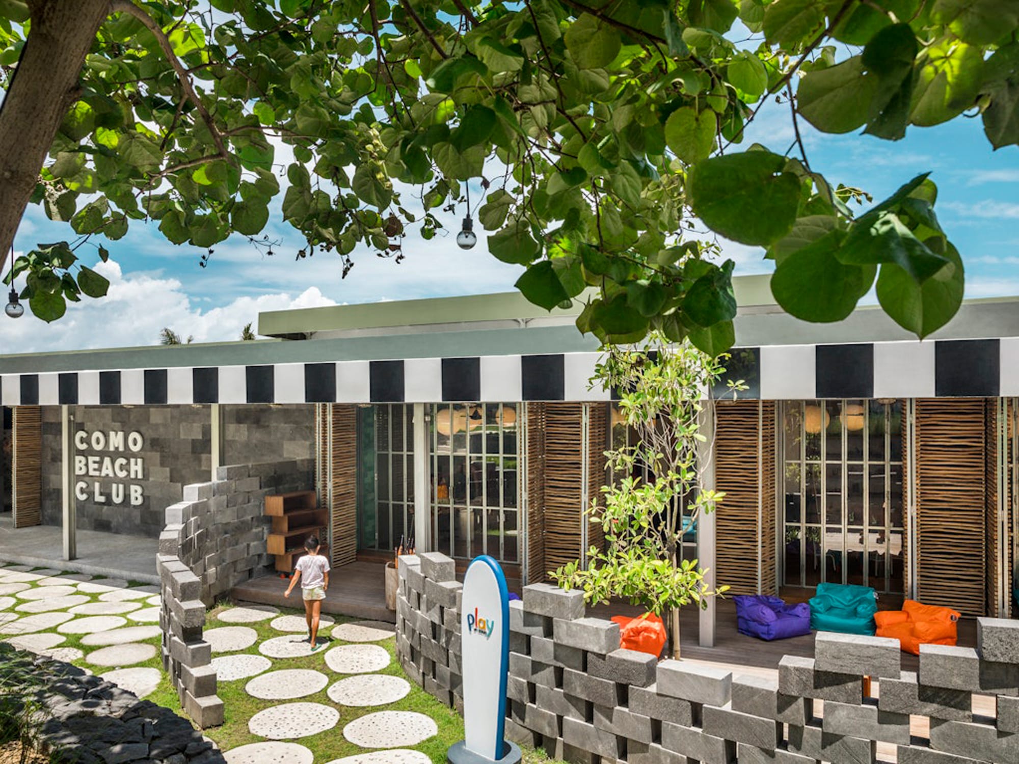 mm978_COMO_Uma_Canggu_2018 Como Beach Club children's play area with modern architecture, stone walls, and colorful bean bags under tropical trees