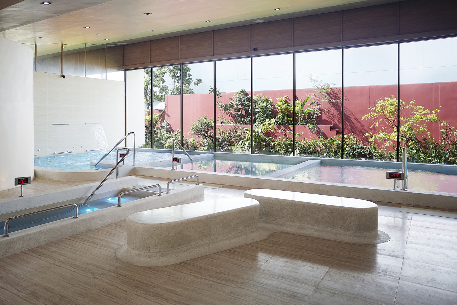RXV_Hydrothertapy_3 Modern spa facility with multiple soaking pools and large windows overlooking red-roofed buildings