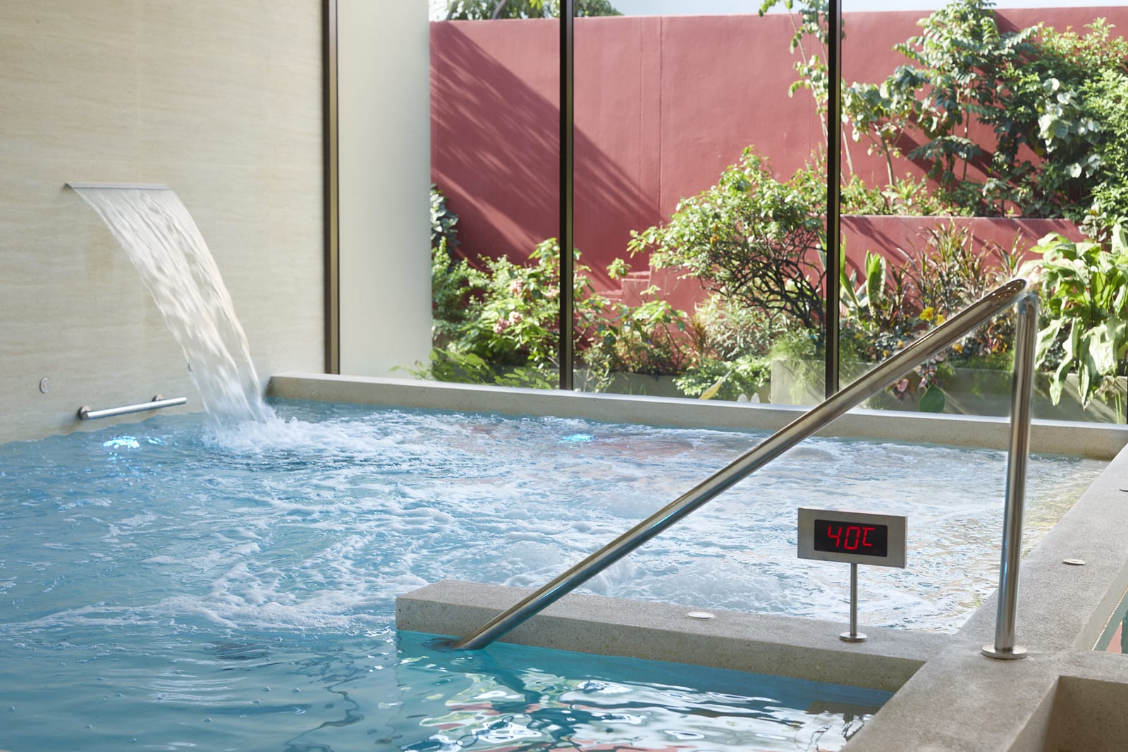 RXV_Vitality Pool Indoor thermal bath with waterfall feature and 40°C temperature display, garden view beyond windows